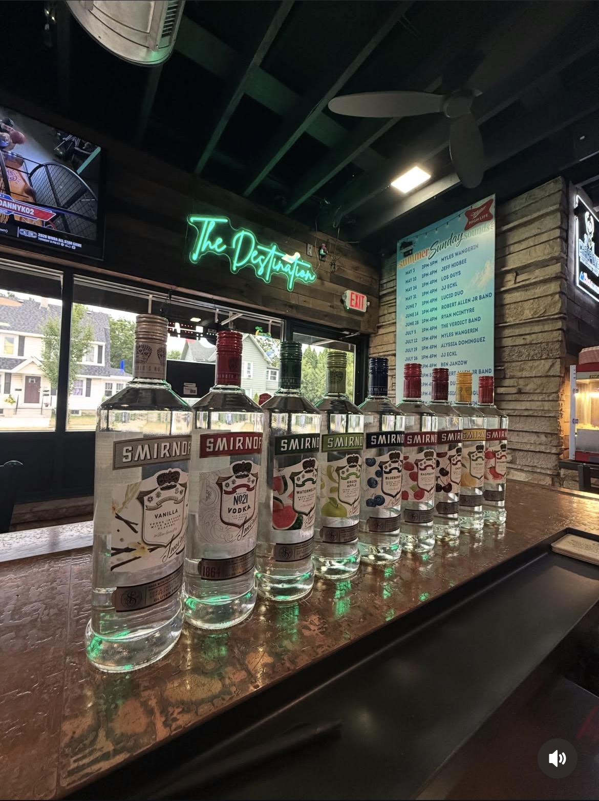 Row of flavored vodka bottles on the bar beneath the green "The Destination" neon sign